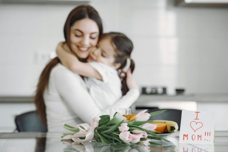 mama i dziecko przytulające się w kuchni, na stole bukiet kwiatów i śniadanie na Dzień Matki